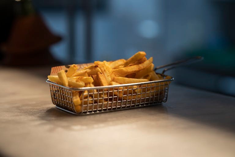 Delicious golden crispy french fries served in a steel basket on a table. Perfect for food photography.